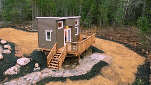 Eine kleine Holzhütte mit einer Holzterrasse, einem Steinweg und Blick auf den umliegenden Wald.