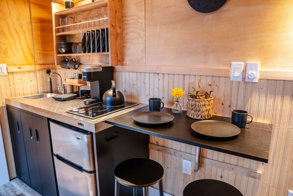 Una cocina moderna con estufa integrada, cafetera y pileta. Hay muebles de madera y una encimera de madera.