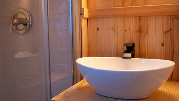 A bathroom with a white vessel sink on a wooden countertop, a glass shower enclosure, and wooden paneling on the walls.