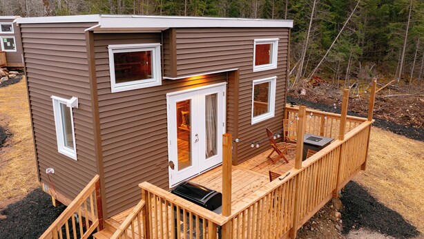 Eine kleine, zweistöckige Holzhütte mit einer Veranda, großen Fenstern und einem Kamin.