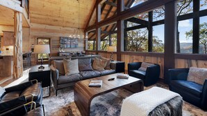 A spacious living area with a wooden ceiling, large windows, and a cozy seating arrangement including a sofa and chairs.