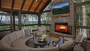 A cozy outdoor seating area with a stone fireplace, comfortable seating, and a scenic mountain view.