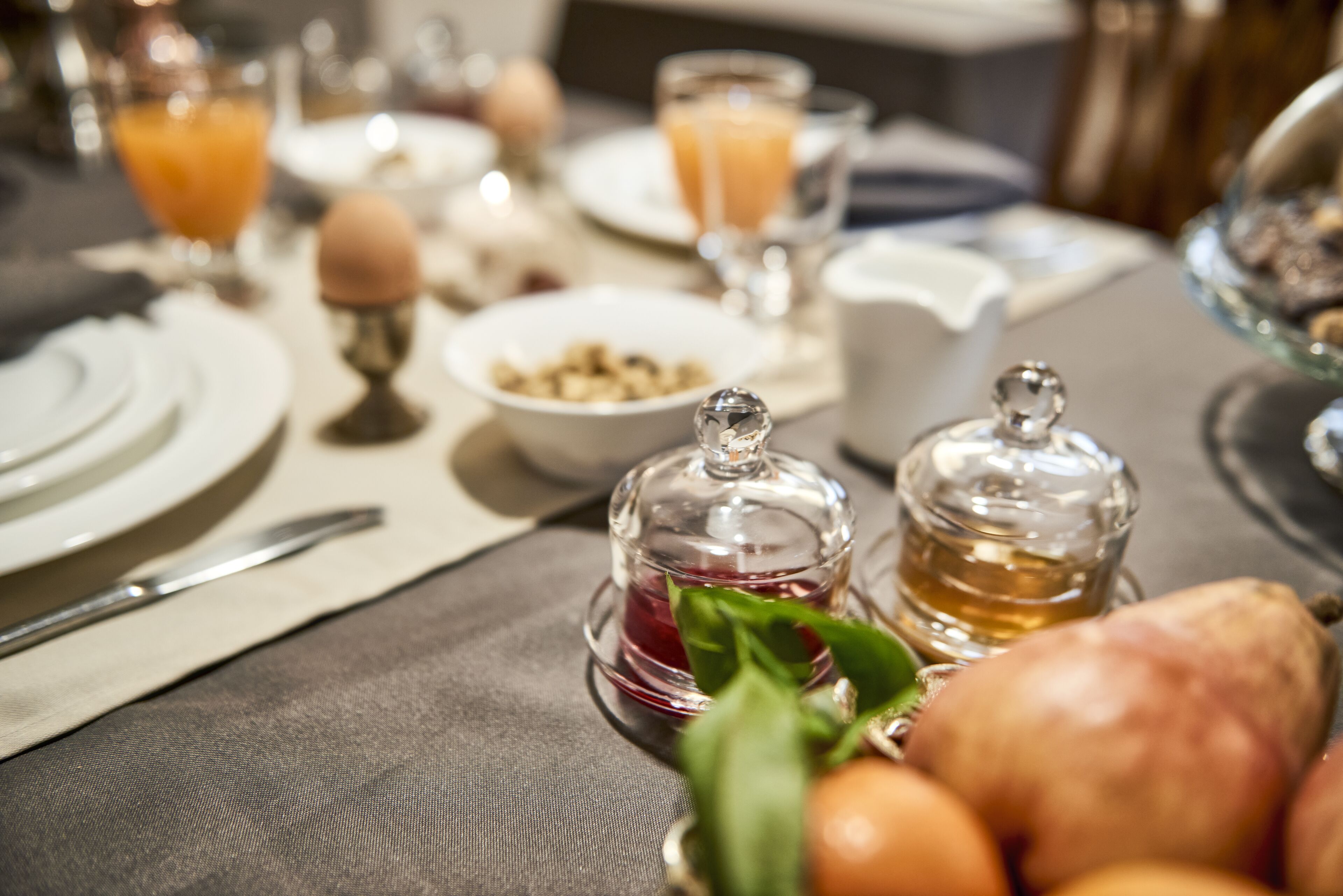 A breakfast setting with a table set for two, including plates, cutlery, glasses of orange juice, a bowl of cereal, and a bread basket.