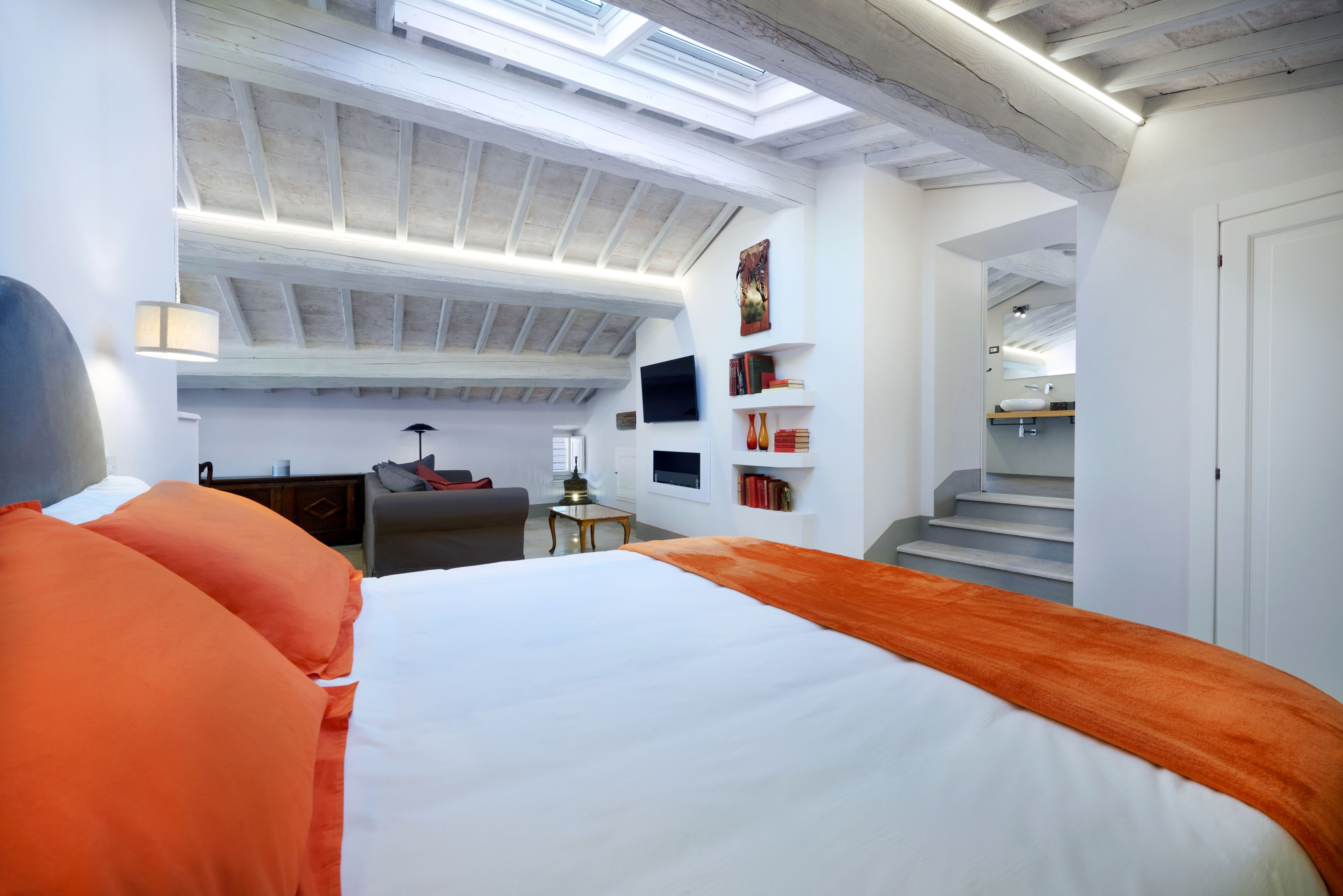 Een moderne slaapkamer met een groot bed, een bureau, een stoel, een televisie en een trap naar een hoger niveau.