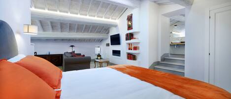 A modern bedroom with a large bed, a desk, a chair, a TV, and a staircase leading to an upper level.