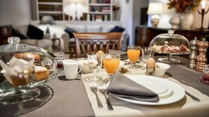 Une table mise pour le petit-déjeuner, avec un présentoir en verre, deux verres de jus d’orange, un bol de céréales et une assiette sur laquelle repose une serviette pliée.