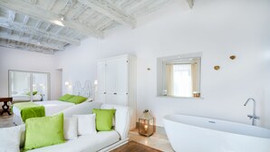 Une chambre d’hôtel moderne aux couleurs claires, avec une grande baignoire, une table basse en bois et un coussin vert qui apporte une touche de couleur.