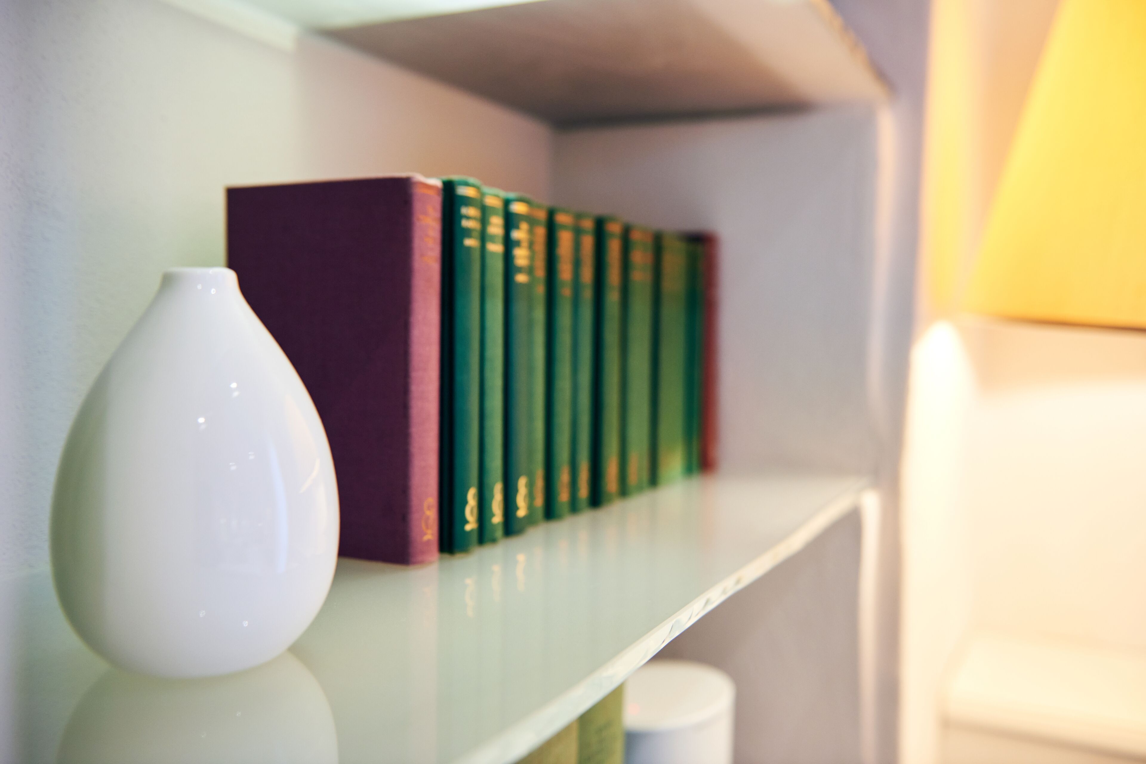 A bookshelf with a white vase and a row of green books.