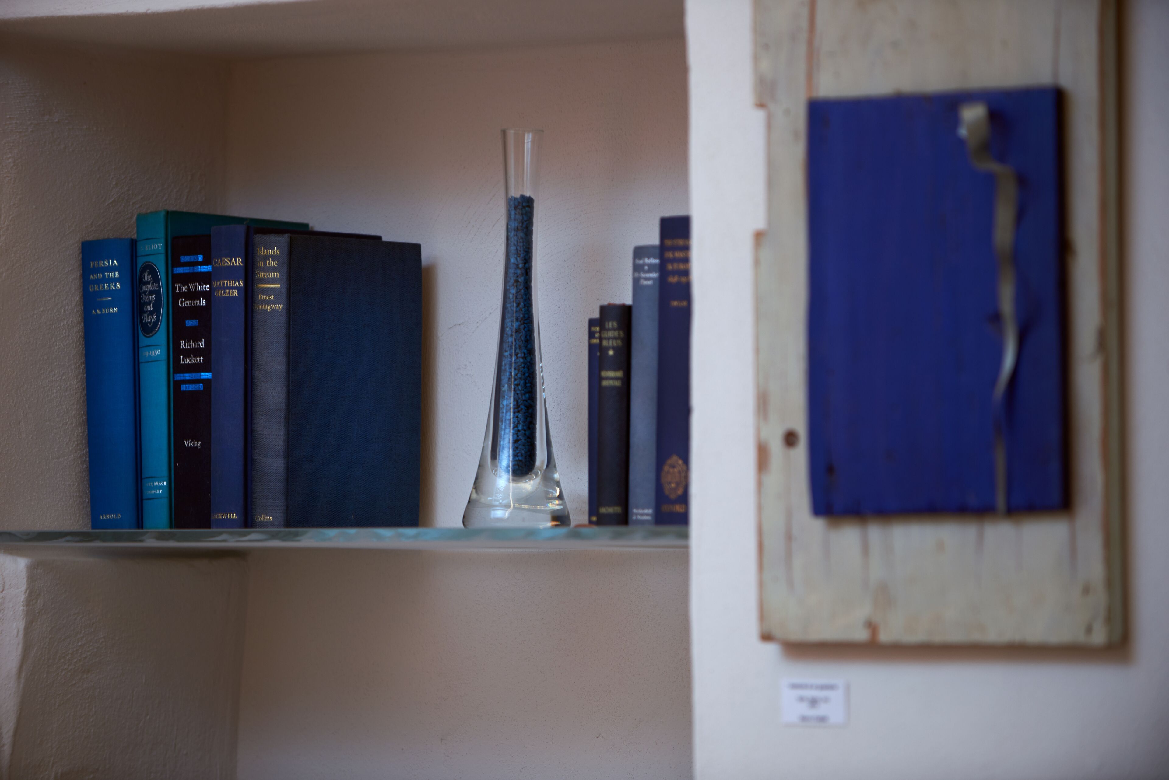 Una estantería con libros y un florero transparente.