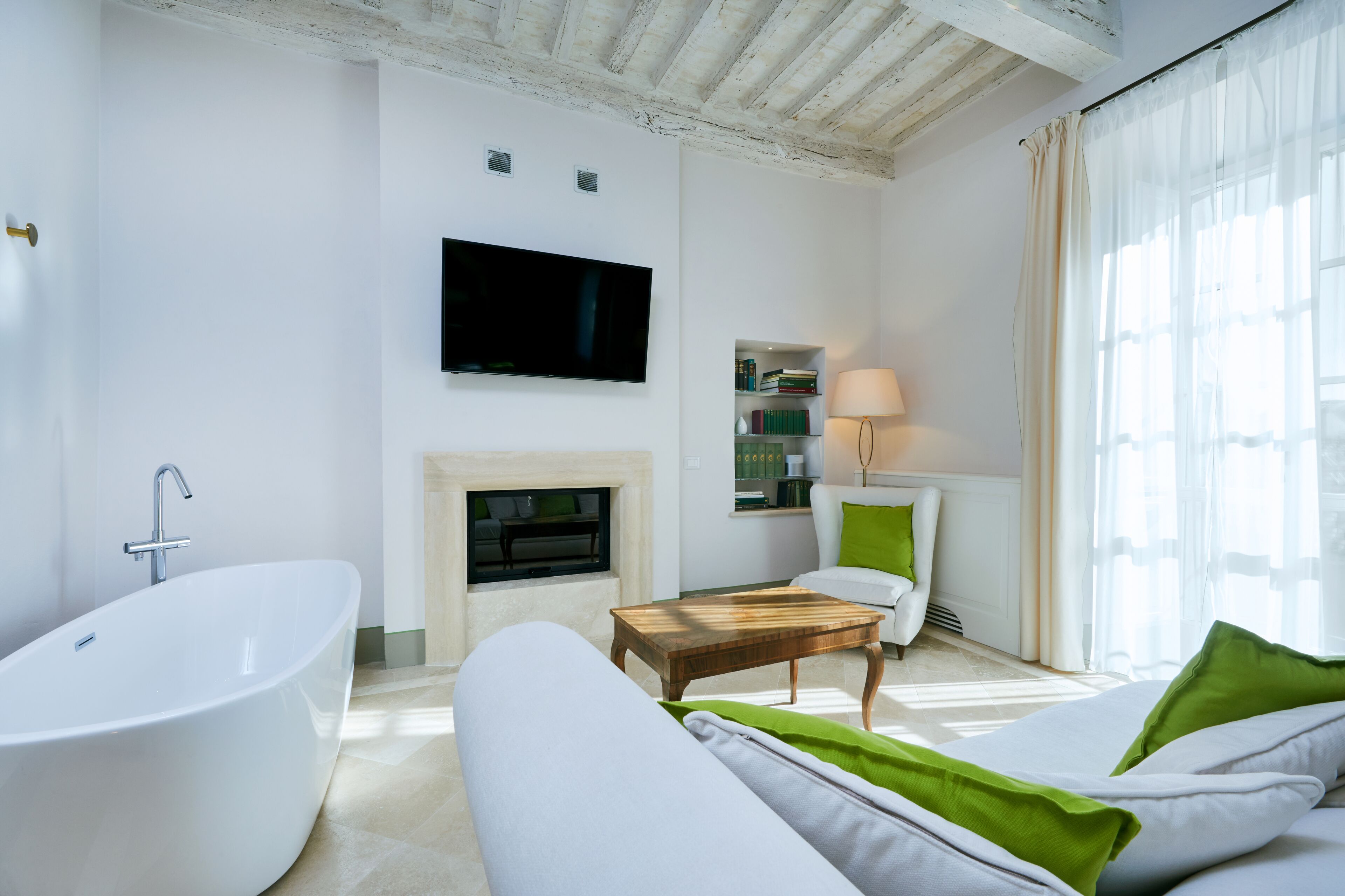 Een moderne woonkamer met een groot bad, een flatscreen televisie aan de muur, een open haard en een bank met groene kussens.