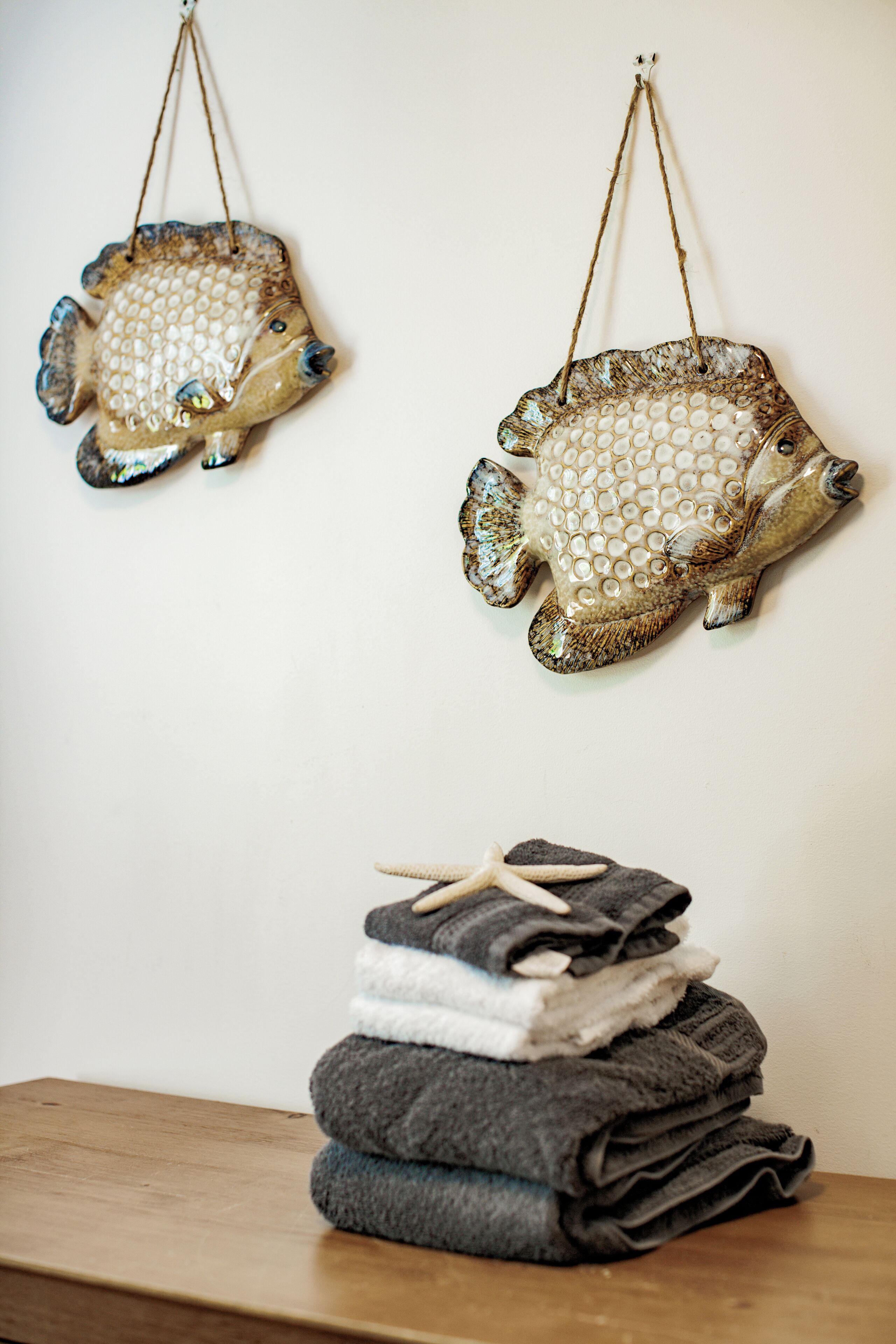 Two decorative fish wall hangings and a stack of folded towels on a wooden surface.