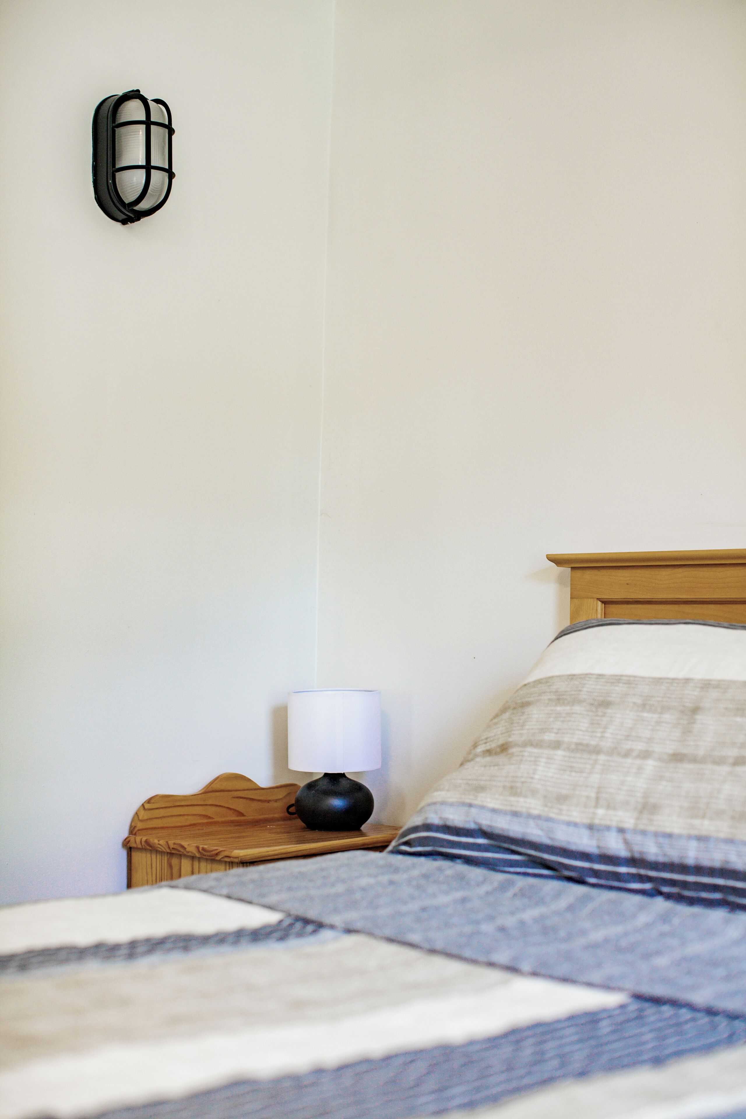 Una cama bien hecha con un edredón a rayas, una lámpara de noche y un aplique de pared.