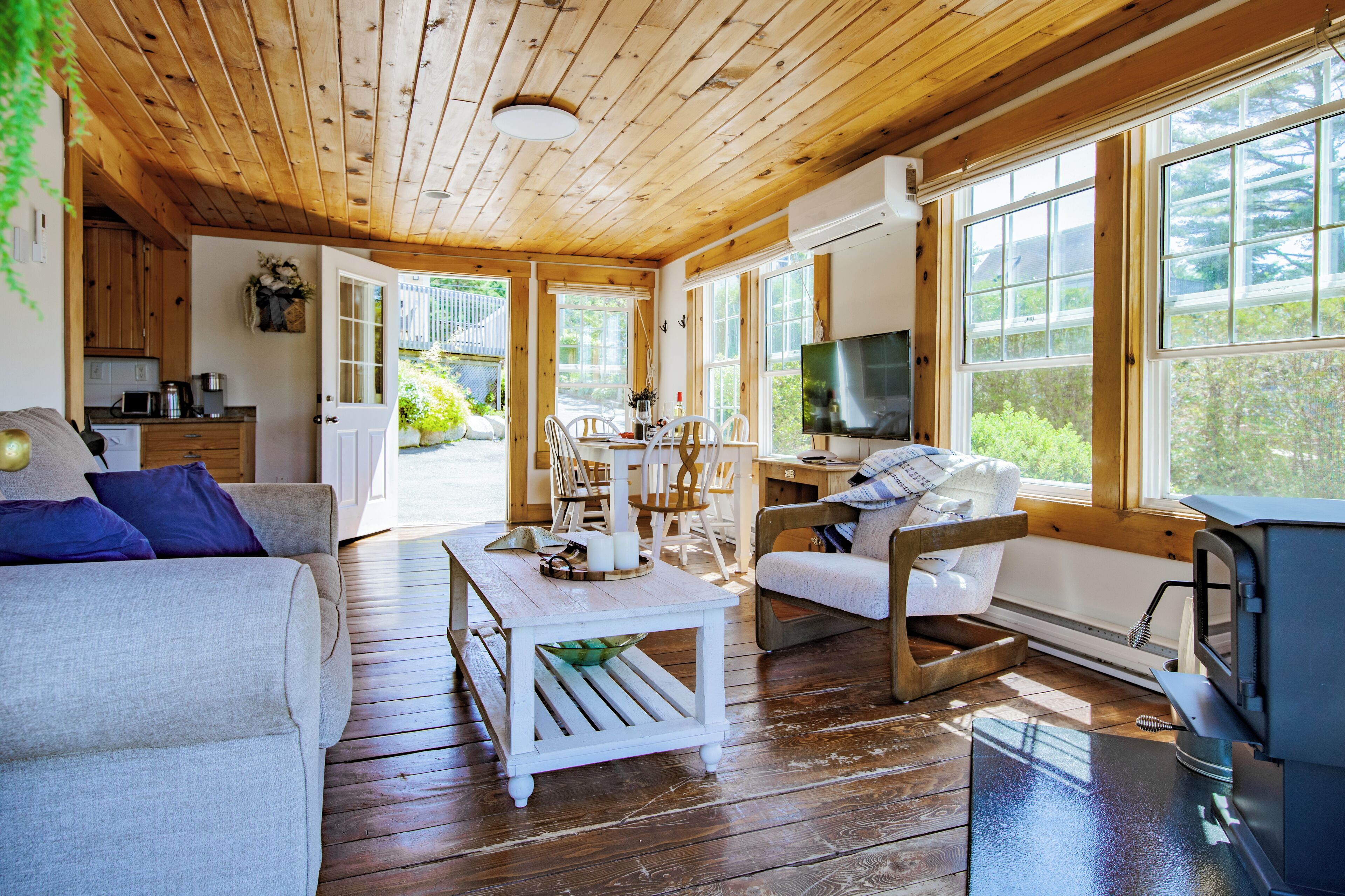 Un acogedor interior de cabaña con pisos de madera, un comedor con mesa y sillas, un sofá, un televisor y una chimenea.
