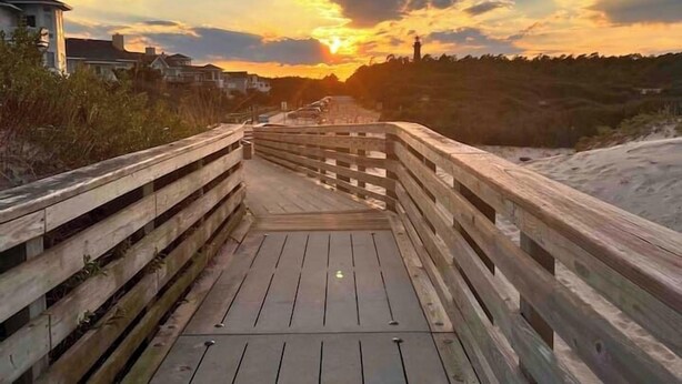 A wooden boardwalk leading to a sunset view with buildings in the background. - Oyster & Pearl Beautiful New Single Level Condo (Corolla)