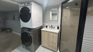 A laundry area with a front-loading washer and dryer, a wooden cabinet with a sink, and a large mirror above the sink.