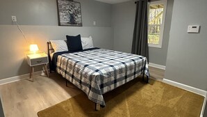 A bedroom with a bed, a nightstand, a lamp, a window with curtains, and a ceiling light.