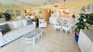 Un salon moderne avec un canapé blanc, une table basse en verre et un coin repas avec des chaises blanches.
