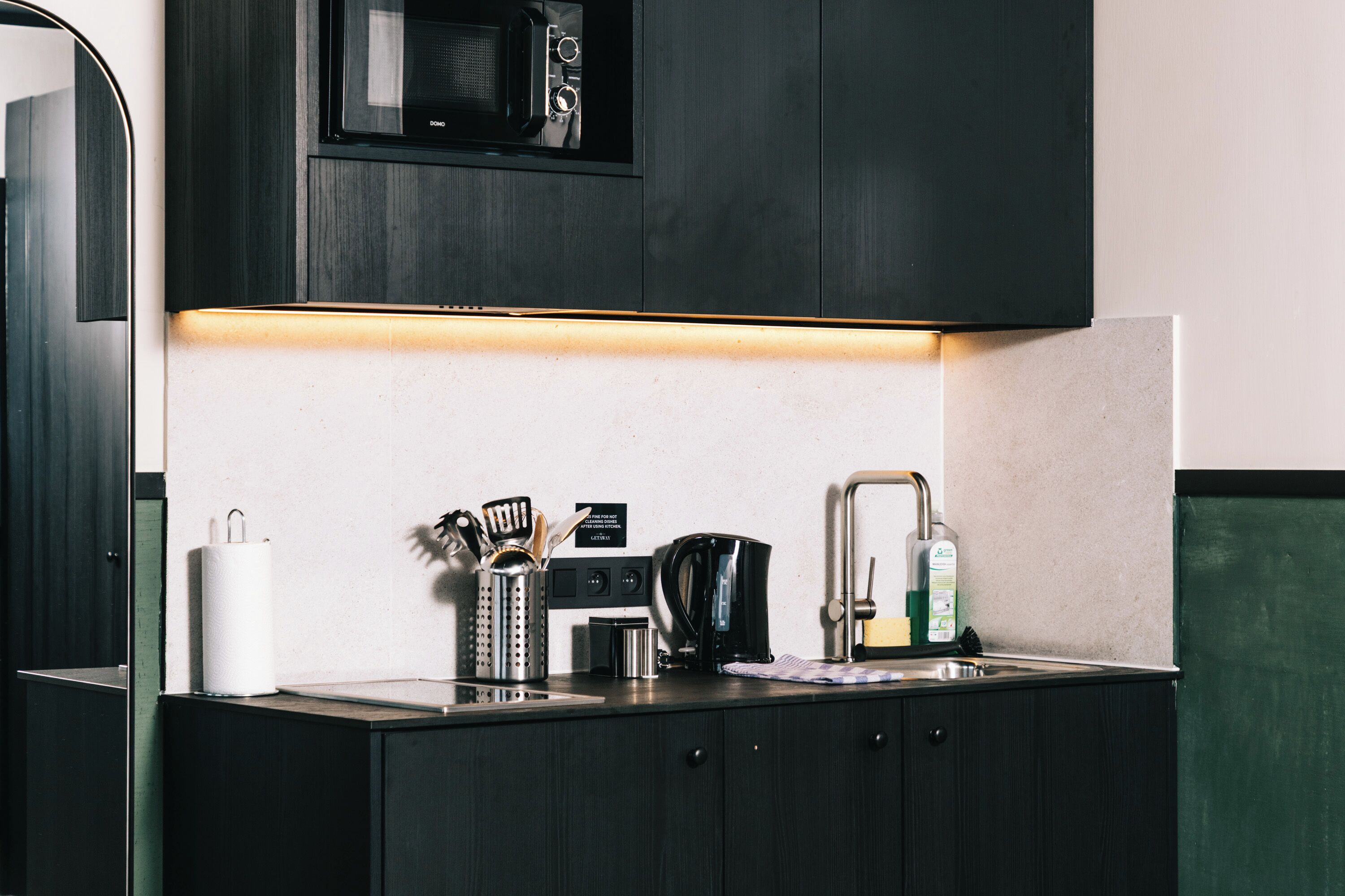 Una cocina moderna con armarios oscuros, un microondas, una cafetera y un lavamanos.