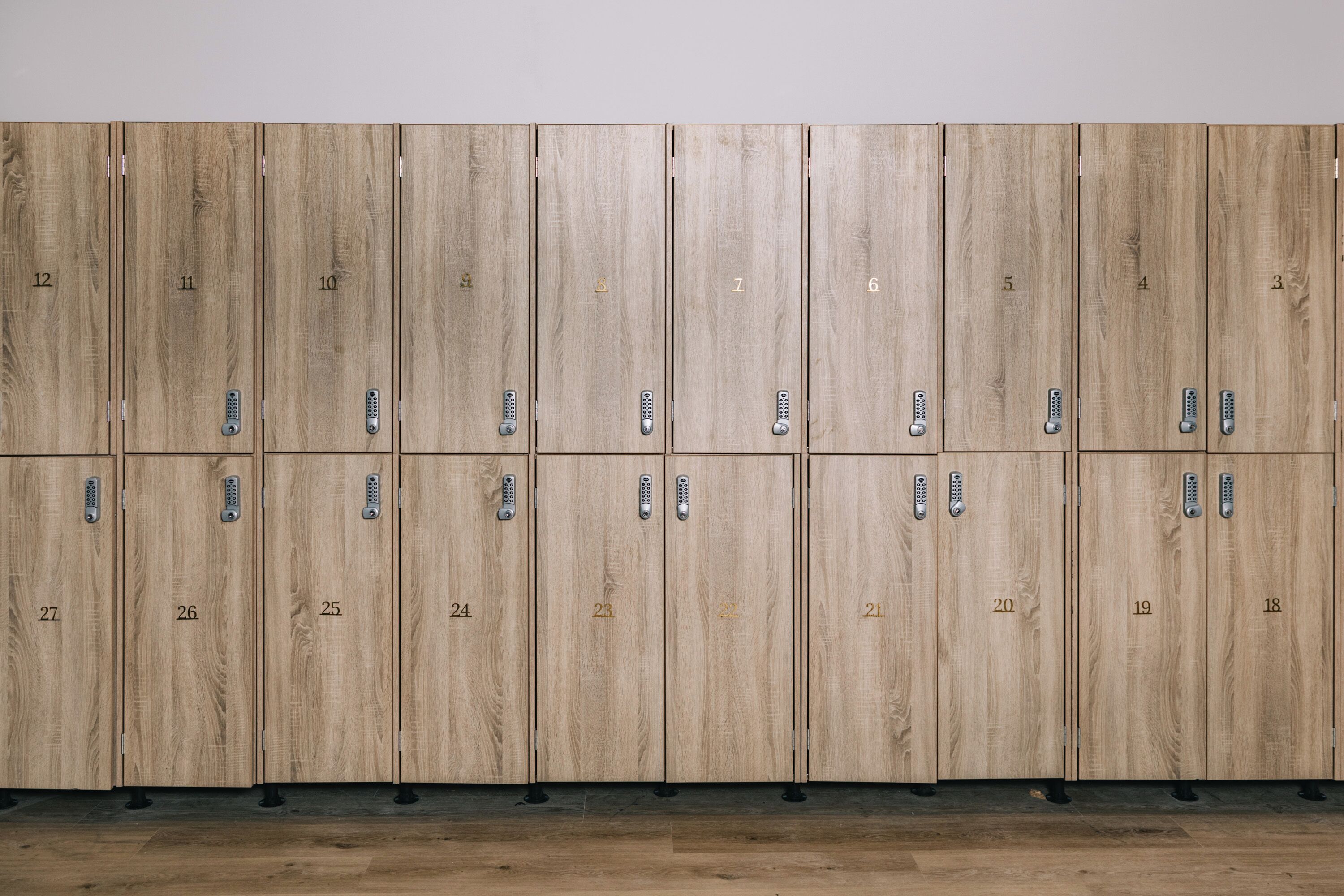 A row of wooden lockers with numbered compartments, each with a keyhole and a small electronic lock.