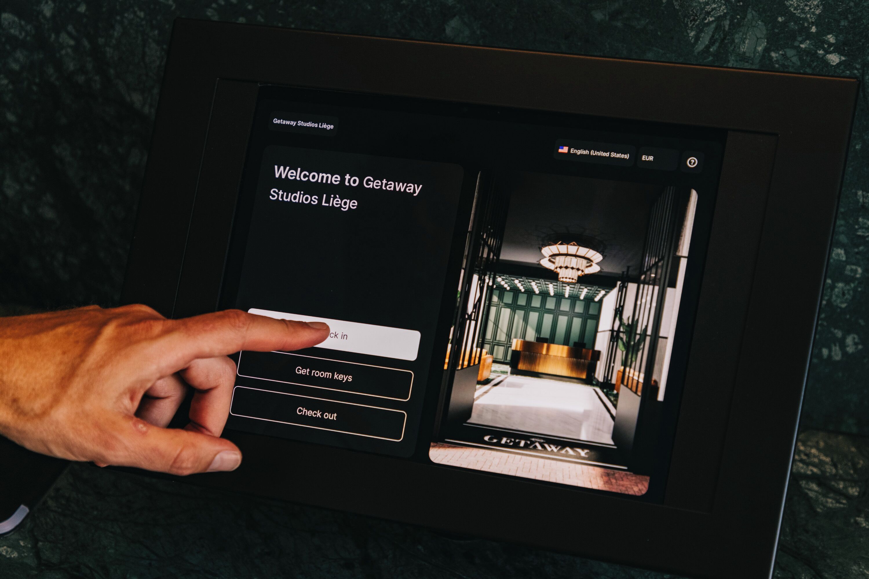 A digital kiosk with a welcome screen for Getaway Studios Liège, featuring a bed and a chandelier.