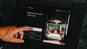 A digital kiosk with a welcome screen for Getaway Studios Liège, featuring a bed and a chandelier.