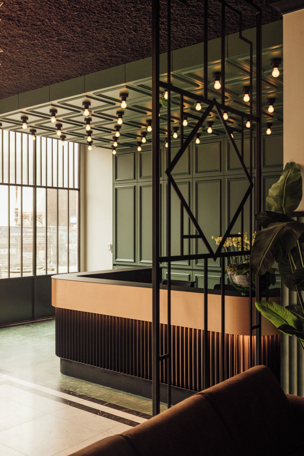 A modern reception area with a geometric light fixture, a reception desk, and a large window offering a view of the city.