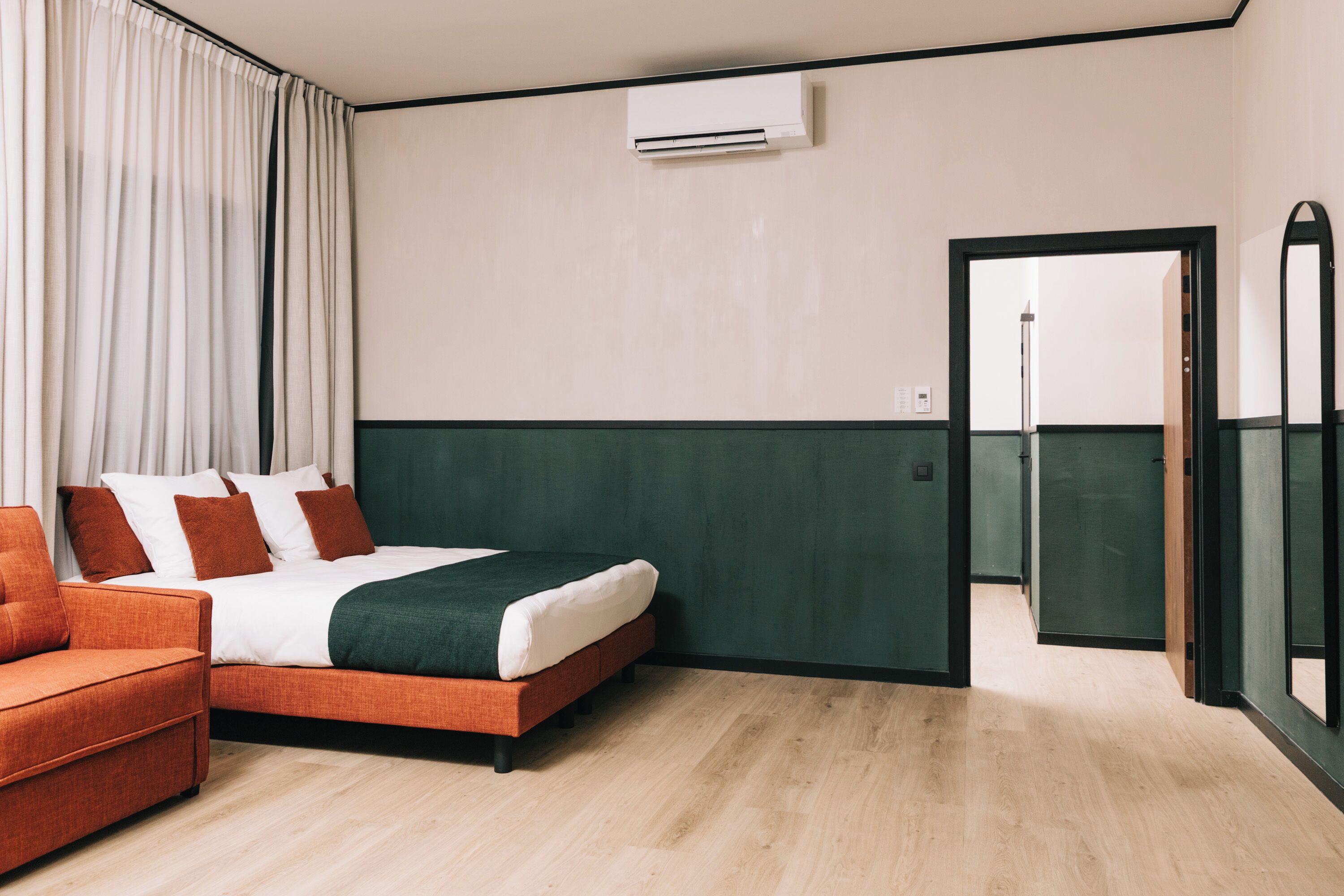Een hotelkamer met een bed, een oranje sofa en een deur naar een andere kamer.