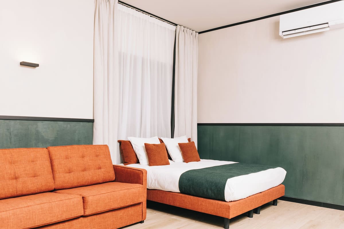 Ein modernes Hotelzimmer mit Bett, orangefarbenem Sofa und einer grünen Akzentwand.