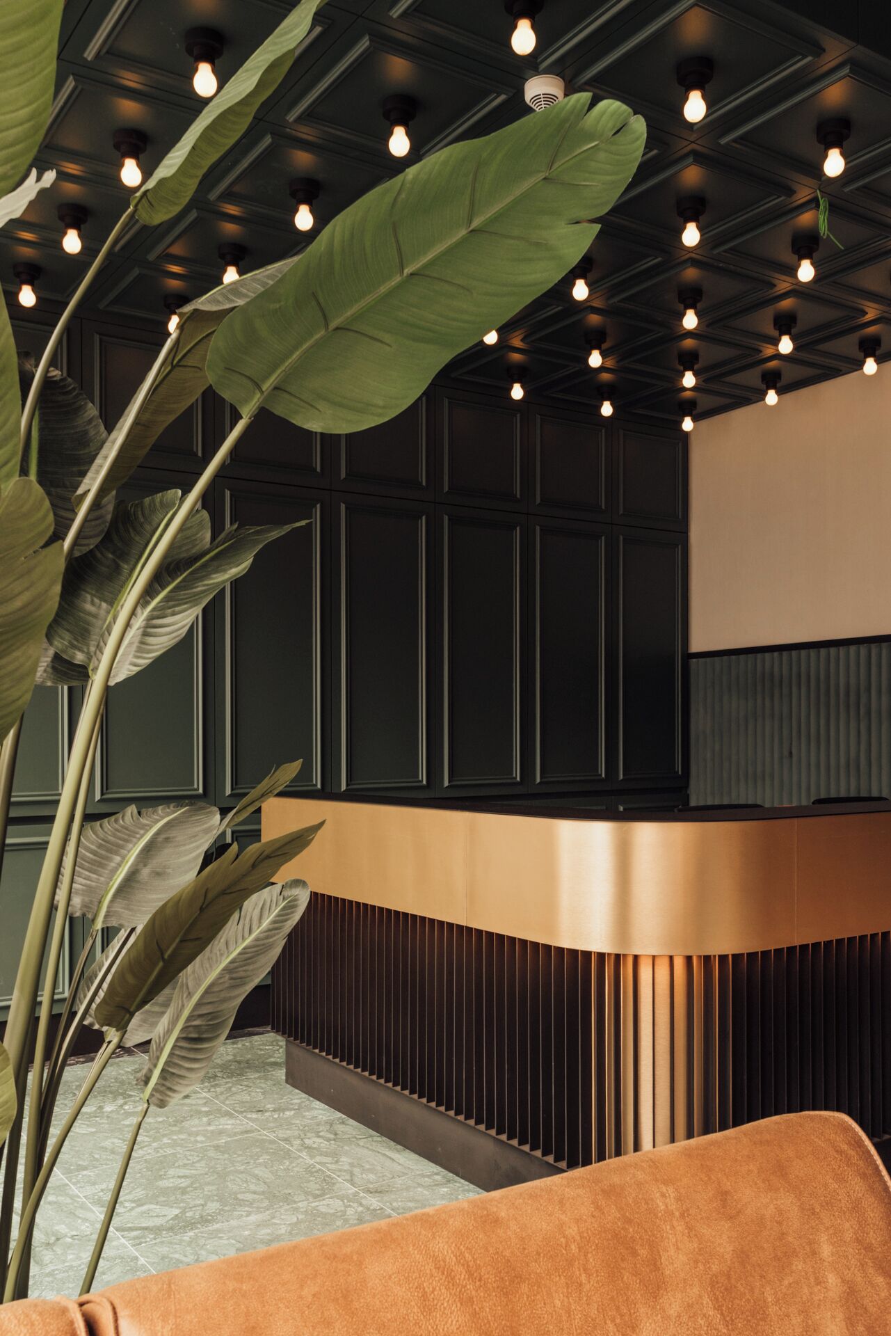 Un área de recepción con un mostrador curvo, una planta grande y un techo con conductos expuestos y luces colgantes.