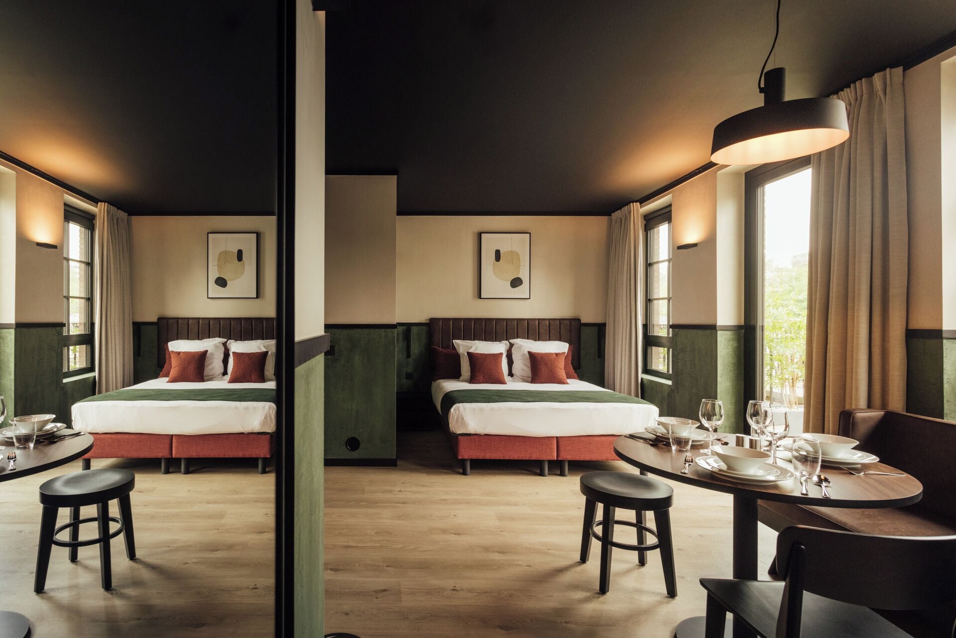 A hotel room with two beds, a dining table with chairs, and large windows.