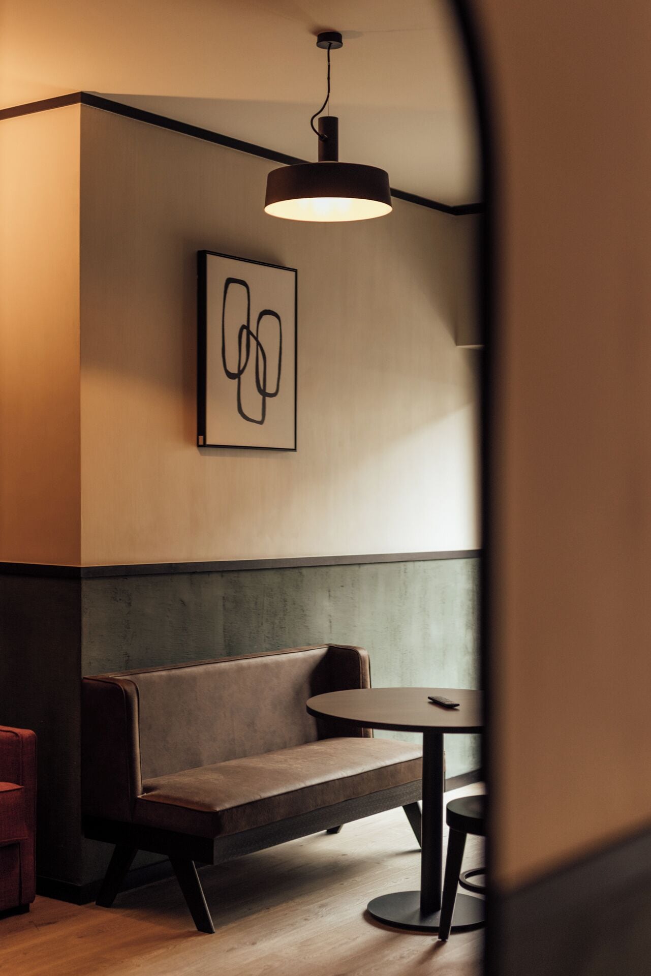Een modern interieur met een bankje en een tafel, een hanglamp en een lijst met abstracte kunst aan de muur.