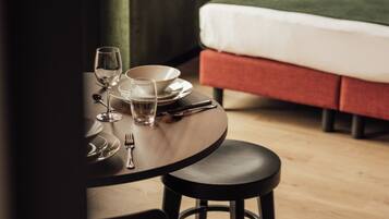 A neatly arranged dining table with a chair, a bed with a red pillow, and a window with curtains in a hotel room.