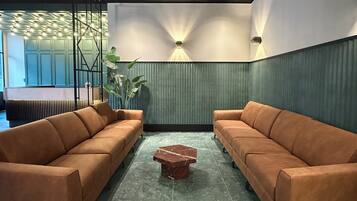 Un lobby moderno con dos sofás marrones, una mesa de centro de mármol y una pared decorativa con iluminación empotrada.