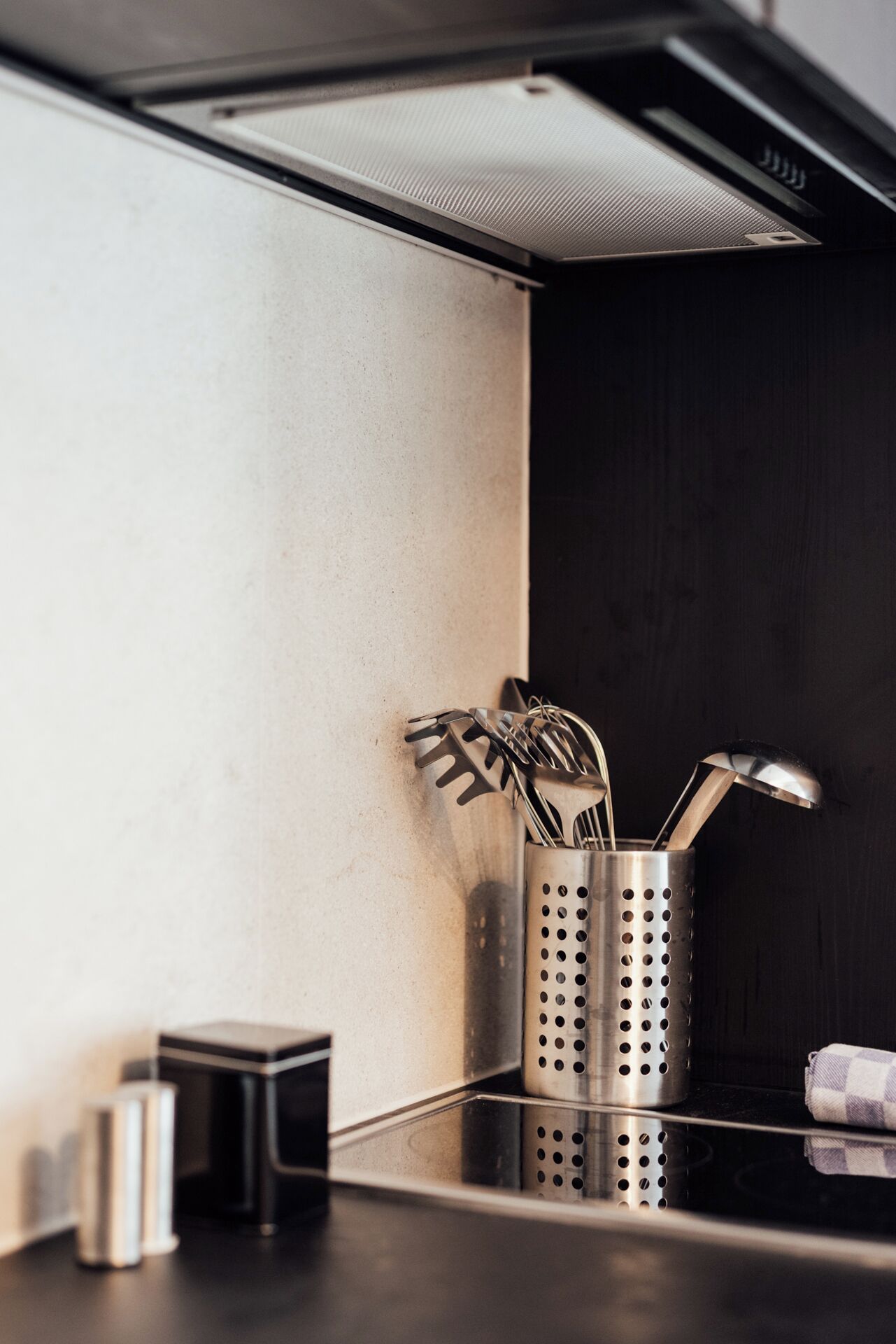 A kitchen with a stainless steel utensil holder on the counter, a small appliance, and a towel.