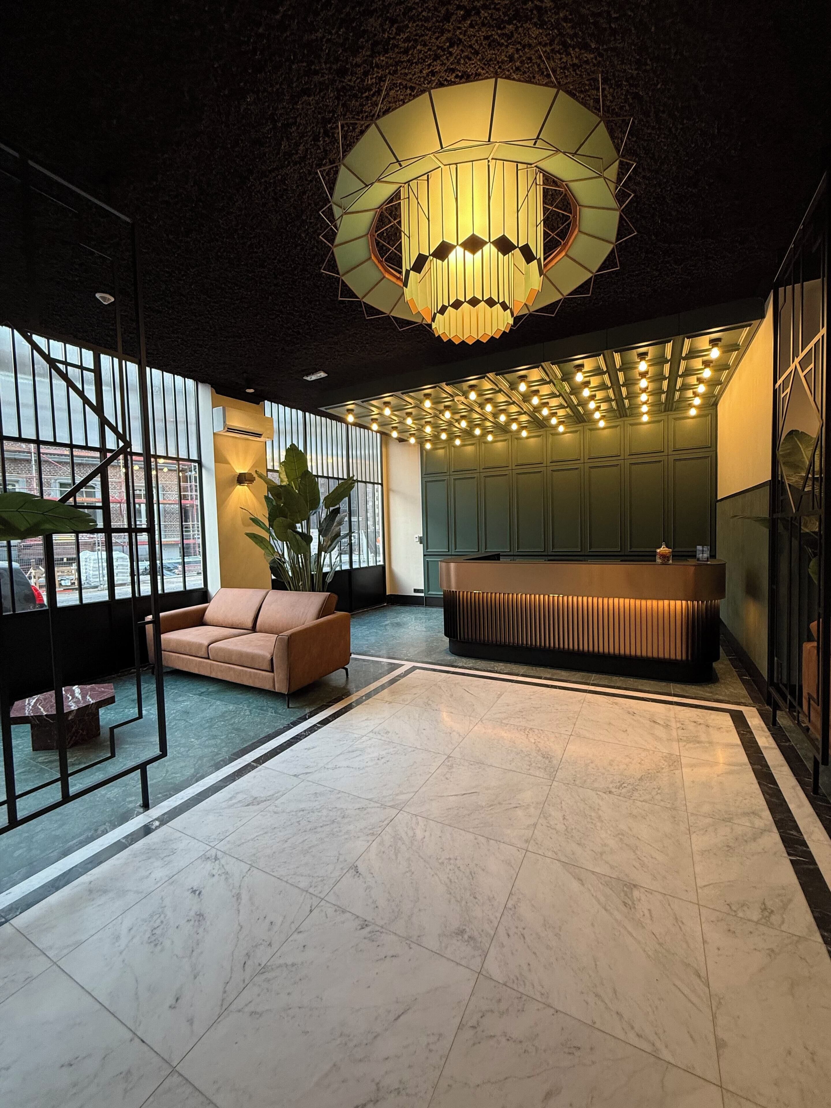 Een moderne lobby met een grote kroonluchter, een receptiebalie en een zithoek met een bank en een lange zitbank.