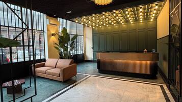 Een moderne lobby met een grote kroonluchter, een receptiebalie en een zithoek met een bank en een lange zitbank.