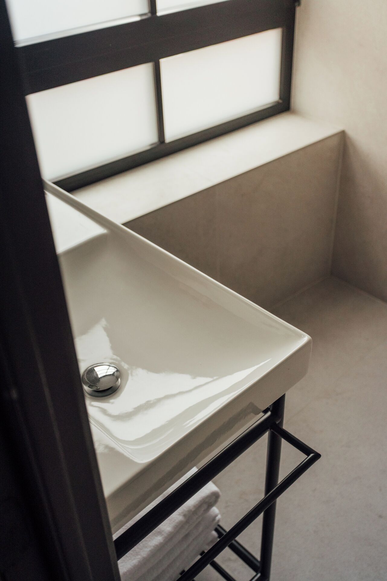 A small bathroom with a white sink, a towel hanging on a rack, and a window above the sink.