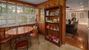 A dining area with a wooden table and chairs, a bookshelf with books and games, and a view of the kitchen through an open doorway. - New Listing! - Bungalow on Belmar, 4 Bed Sleeps 6. Walk to Lake Hollingsworth!  (Lakeland)