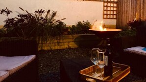 En udendørs patio med et bord, to stole, et lys og en flaske.