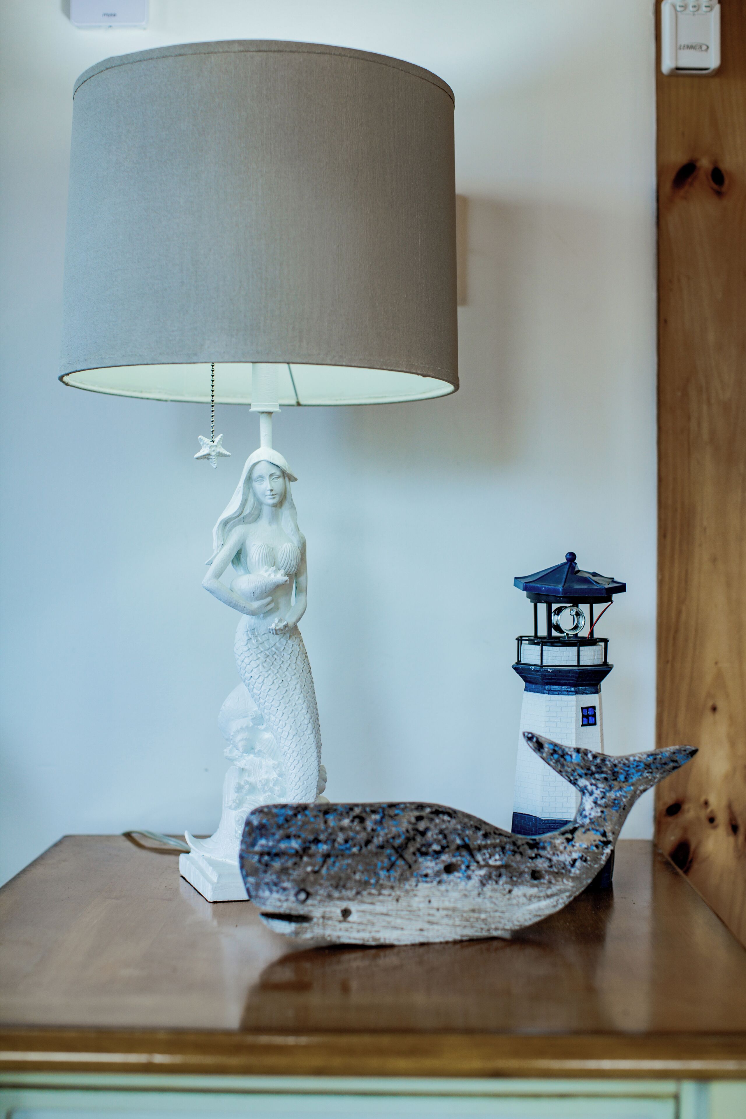 A table with a lamp, a mermaid sculpture, and a lighthouse model.