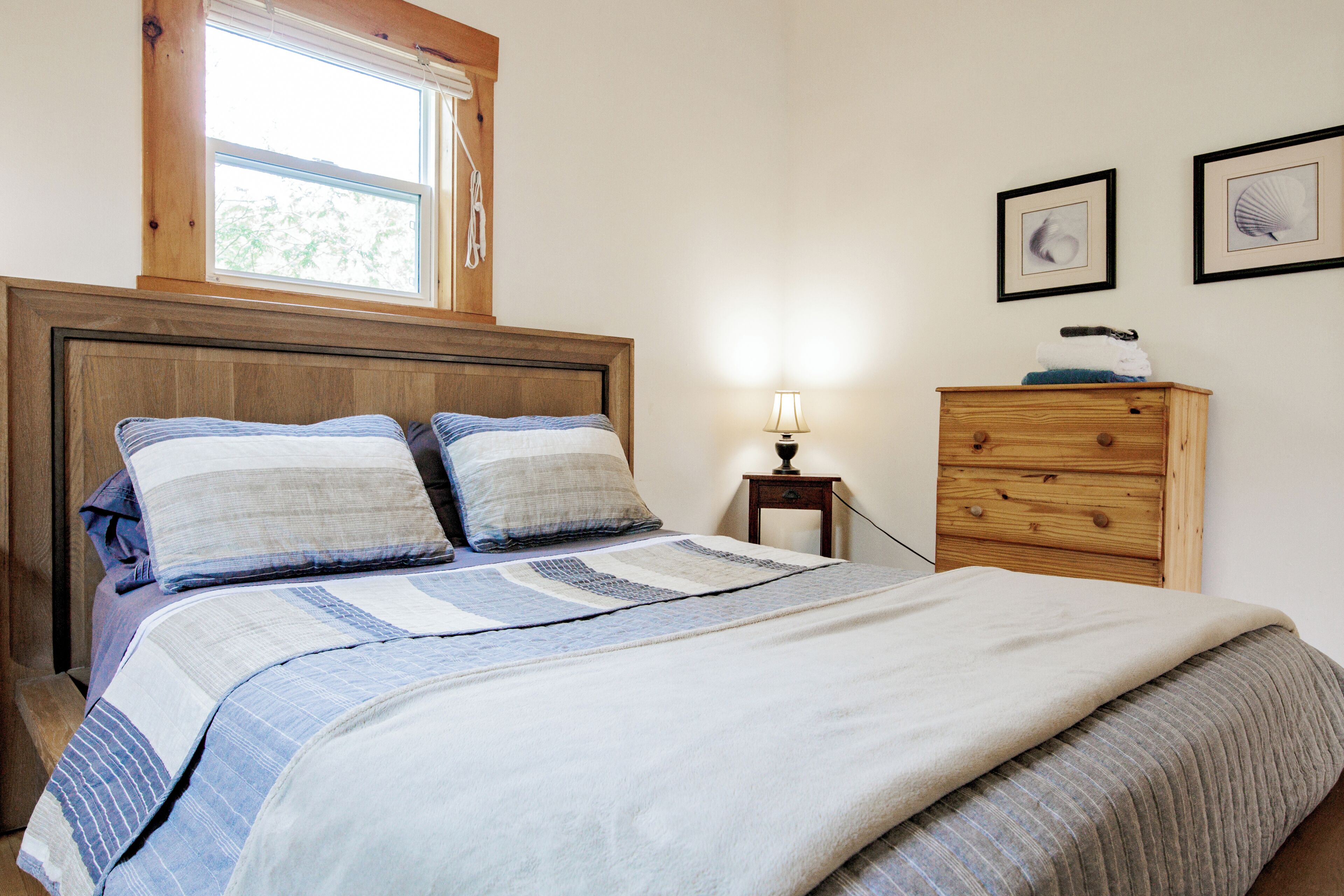 Un dormitorio con una cama de madera, una mesita de noche con una lámpara, un aparador y dos cuadros enmarcados en la pared.