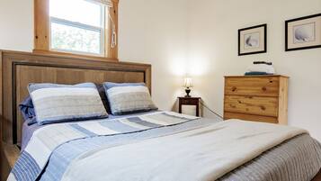 Un dormitorio con una cama de madera, una mesita de noche con una lámpara, un aparador y dos cuadros enmarcados en la pared.