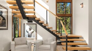 A modern staircase with wooden steps and black railings, leading to a second floor. There are two white armchairs and a small table in the foreground. - Suncadia's #1 6BR/6BA Luxury Retreat! Huge Swim Spa*Hot Tub*Game Room*5 Mstrs (Cle Elum)