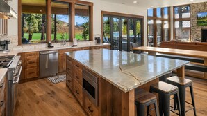 A modern kitchen with wooden cabinets, a large island, and a stone fireplace. - Suncadia's #1 6BR/6BA Luxury Retreat! Huge Swim Spa*Hot Tub*Game Room*5 Mstrs (Cle Elum)