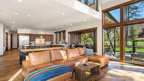 A spacious living area with a leather sofa, a coffee table, and large windows offering a view of the outdoors. - Suncadia's #1 6BR/6BA Luxury Retreat! Huge Swim Spa*Hot Tub*Game Room*5 Mstrs (Cle Elum)