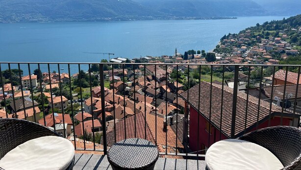 A balcony with wicker chairs and a view of a lake, mountains, and a town. - Amazing Lage View Apartment With Pool and 2 Terraces (Calozzo)