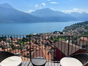 Een balkon met rieten stoelen en uitzicht op een meer, bergen en een stad.