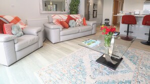 A modern living room with two sofas, a coffee table, and a kitchen area visible in the background. - Little Roskrow (Penryn)