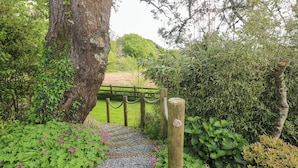 A garden pathway leading to a wooden gate surrounded by lush greenery and flowering plants. - Little Roskrow (Penryn)