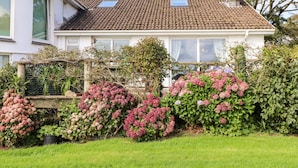 A house with a tiled roof, a satellite dish, and a garden with pink hydrangeas. - Little Roskrow (Penryn)
